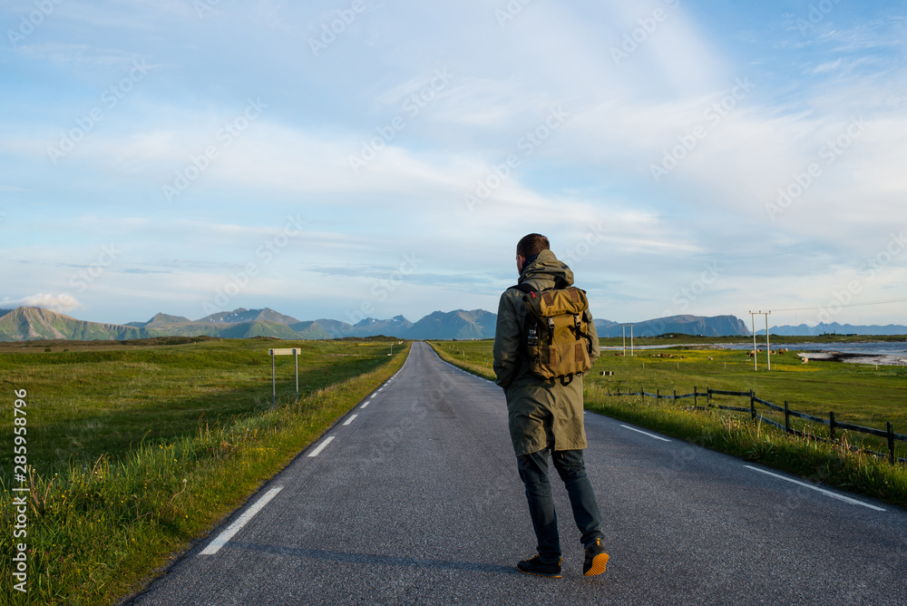 Man with backpack walking on an empty road. Amazing landscape, mountain and ocean. Scenic view. New way. Enjoy the moment, relaxation. Wanderlust. Travel, adventure, lifestyle. Explore North Norway