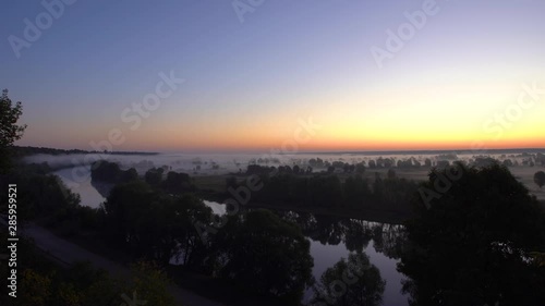 Great scenic early morning foggy landscape of blue sky beafore sunrise, green dark trees and foggy surface of river. Real time 4K video footage. photo