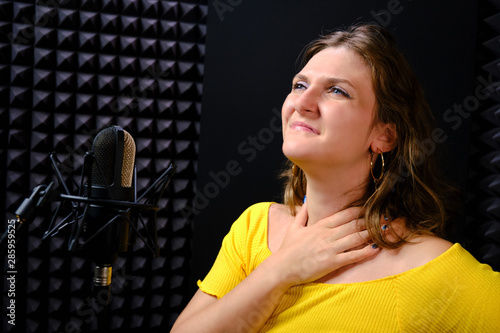 A young woman holding her throat near the microphone, black background. The voice of the singer when recording a song in the music Studio. Voice failure, hoarseness, pain in the vocal cords. photo