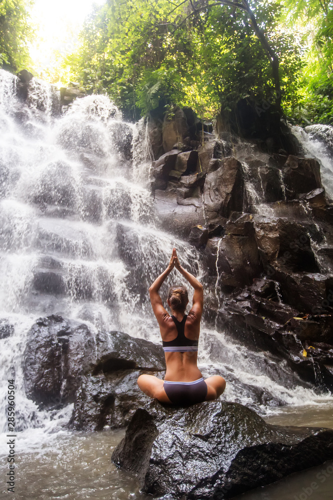 Woman practices yoga near waterfall in Bali, Indonesia Woman practices yoga near waterfall in Bali, Indonesia