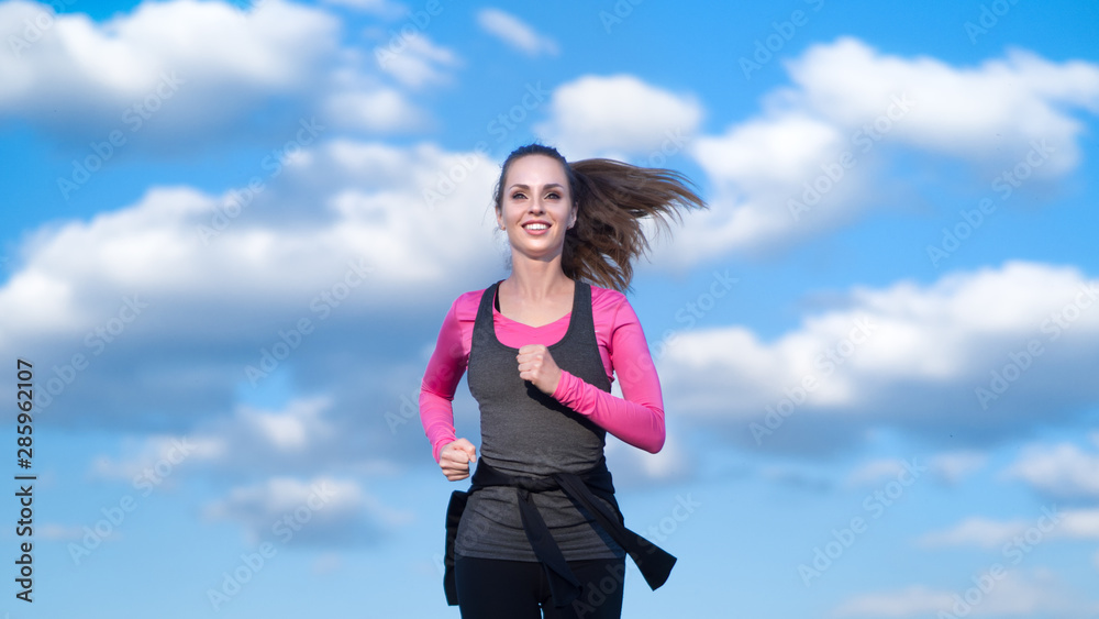 Woman jogging on the blue cloudy sky background. Woman jogging on the blue cloudy sky background.