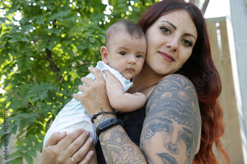 Portrait young happy mother lovingly holds in her arms her 2-month-old son, a newborn, cute baby. Happy motherhood. Girl with a tattoo on her arm.