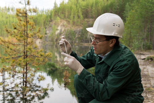 industrial ecologist takes a sample of water from a flooded quarry photo
