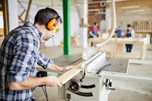 Back view portrait of mature carpenter cutting wood in joinery workshop, copy space