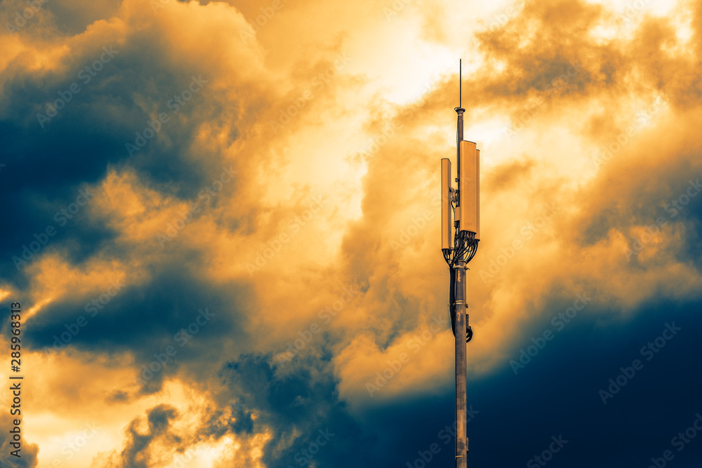 Fototapeta premium A column with transmitters and mobile telephony antennas against the sky with clouds at sunrise
