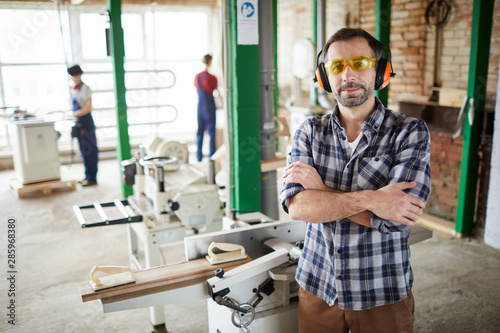 Waist up portrait of confident mature carpenter standing with arms crossed in workshop  copy space