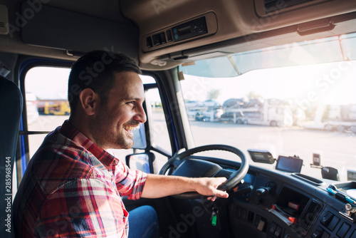 Professional middle aged truck driver in casual clothes driving truck vehicle going for a long transportation route.