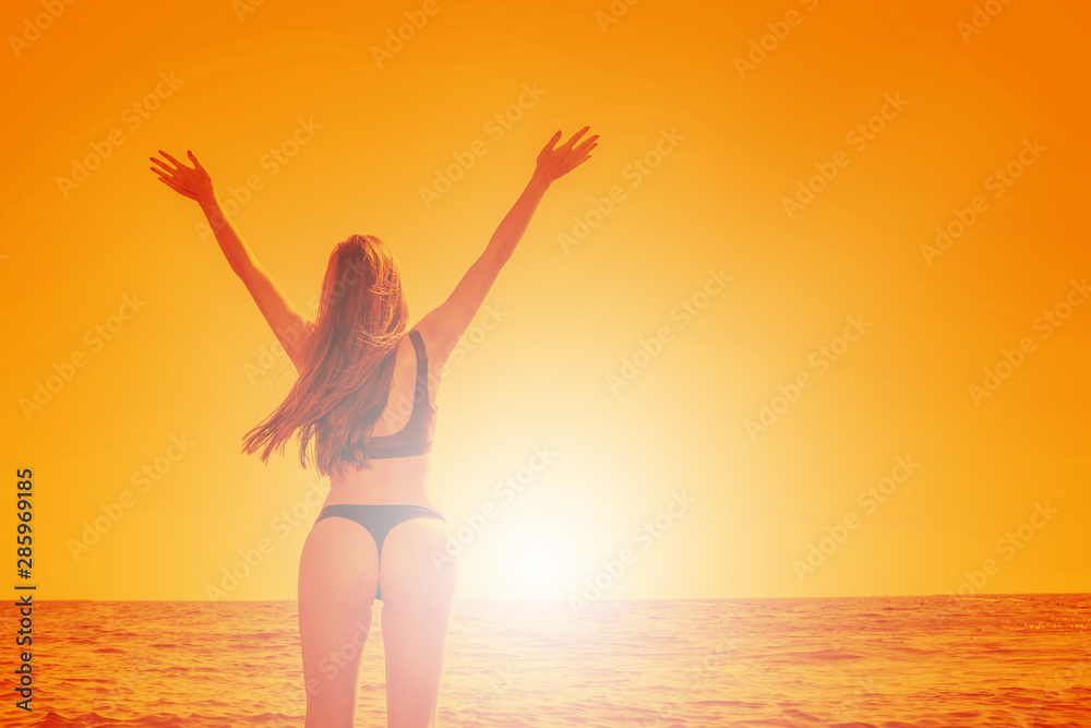 A young girl in a swimsuit stands on the beach with her hands up towards the summer sun. A young girl in a swimsuit stands on the beach with her hands up towards the summer sun.