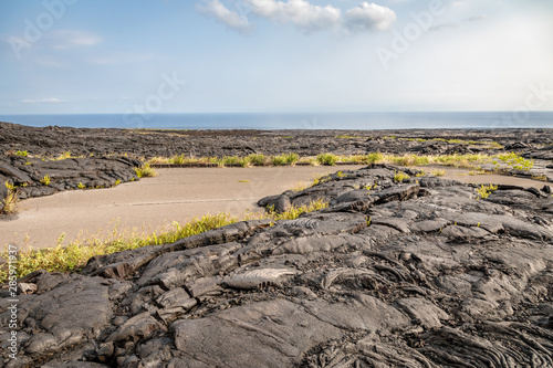 A small piece of road is not consumed by the cold dark lava rock in the lava fields near Holei Pali on the big Island of Hawaii photo