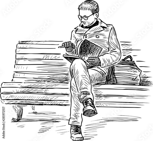 Young townsman sits on park bench and reads a book