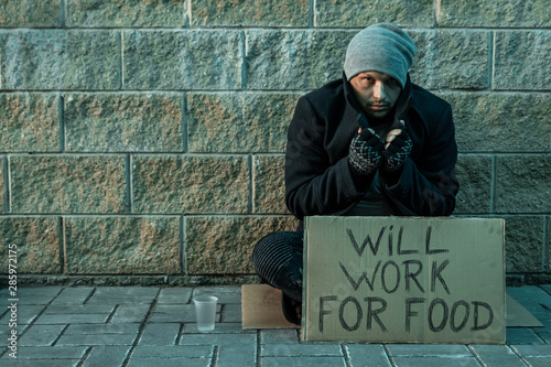 A man, homeless, a man asks for alms on the street with a sign will work for food. Concept of homeless person, addict, poverty, despair.