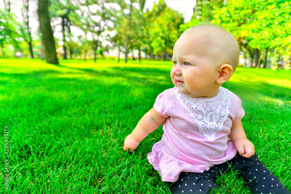 Little girl sitting on green grass, close up.