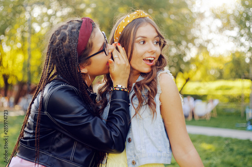 Two friends share secrets. Sisters gossip. Girl whispering a secret to her ear in ear. Two beautiful brunettes at sunset.