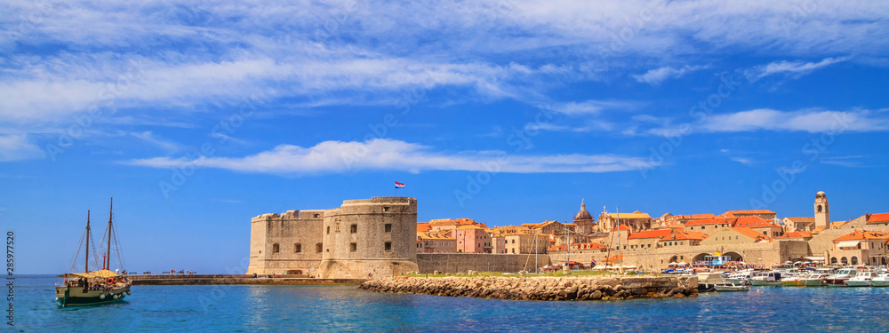 Coastal summer landscape, banner - view of a sailboat and the City Harbour of the Old Town of Dubrovnik on the Adriatic coast of Croatia