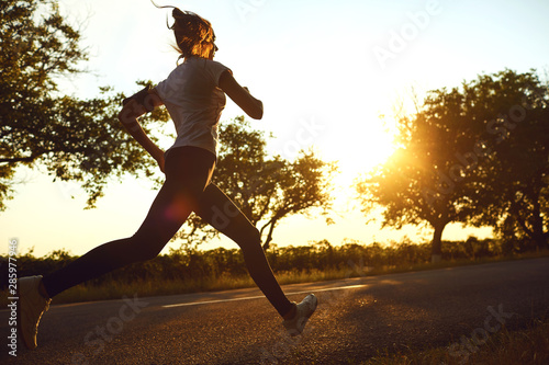Girl runner runs on the road the sun at dawn.