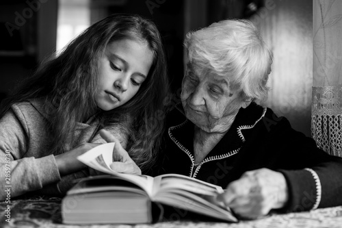 Child of eleven with his grandmother together reading a book. Black and white photo.