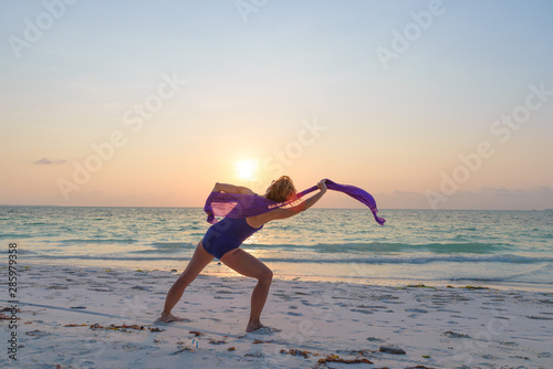 Woman performing yoga exercise on sand beach romantic sky at sunset, rear view, golden sunlight, real people