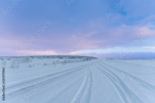Tire tracks on snow covered road in an Arctic landscape under a cloudy evening sky above the Arctic Circle © Niccolo