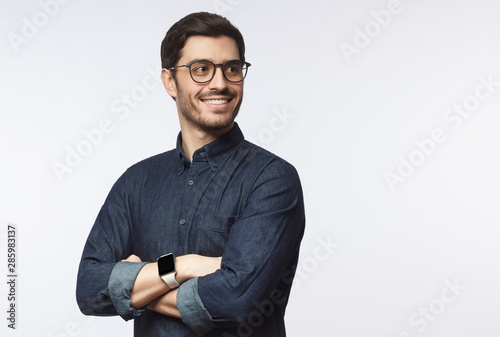 Young handsome business man dressed in casual denim shirt with smartwatch on wrist, isolated on gray background photo