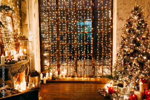 warm cozy magic evening in luxury old Christmas living room fairy tale interior design, fireplace, windows, Xmas tree decorated by lights, gifts, candles, lanterns, garland lighting.New year holiday