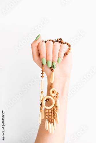 Female hand with green manicure holding wooden necklace.