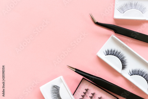 Tools for eyelash extension on trendy pastel pink background. False eyelashes and tweezers. Beauty shop. Makeup cosmetics. Top view, flat lay. Place for text photo