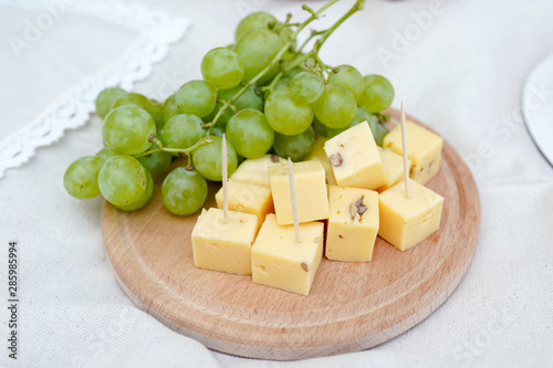 cheese and grapes on a wooden board on white background. picnic food