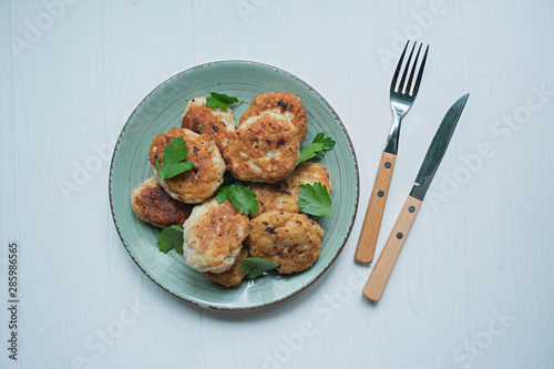 Cutlets with herbs served on a plate on a white wooden background.
