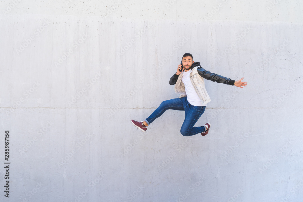 Latin American Man Jumping Excited on a Wall Background While Making a Call