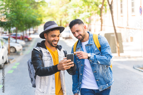 Two Male Friends Walking Together in the Street While Using Cell Phone.