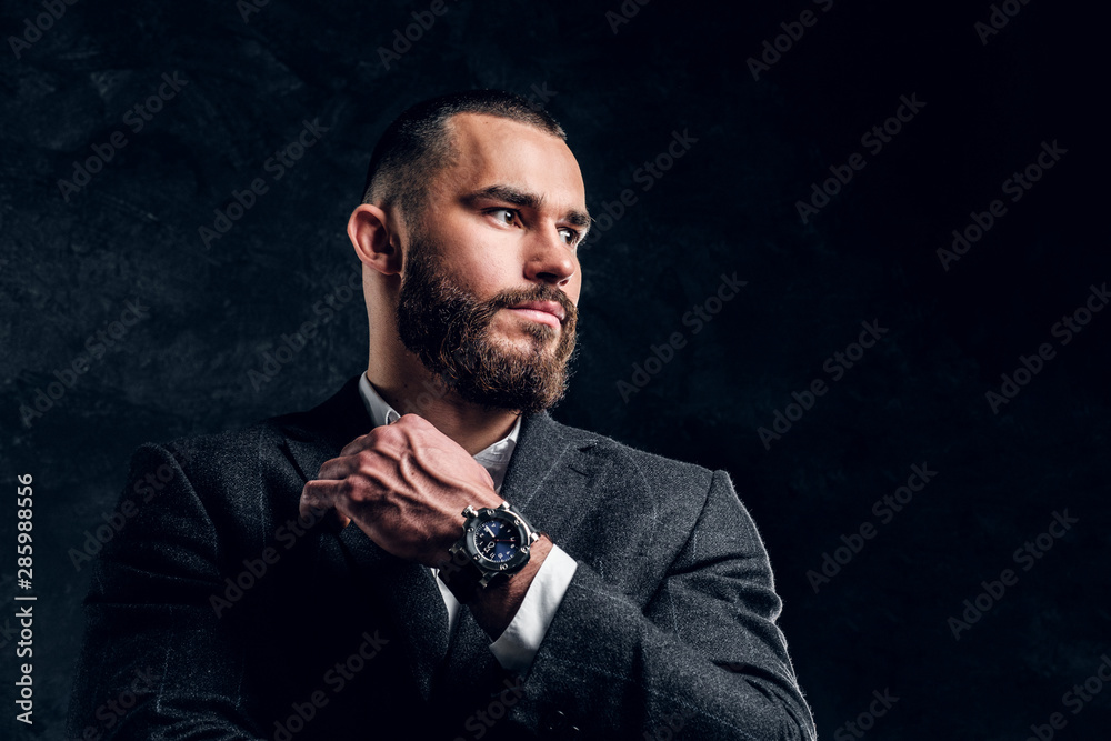 Serious sceptical buisnessman with beard and in dark clothing is standing at dark photo studio. Serious sceptical buisnessman with beard and in dark clothing is standing at dark photo studio.