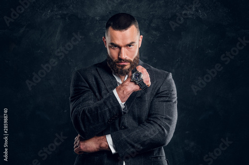 Sucessful serious man is posing for photographer with watch on his fist on the dark background.