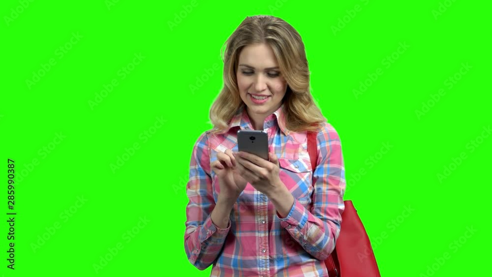 Smiling girl using phone on green screen. Young caucasian woman checking social apps with smartphone. Mobile addiction concept. Smiling girl using phone on green screen. Young caucasian woman checking social apps with smartphone. Mobile addiction concept.