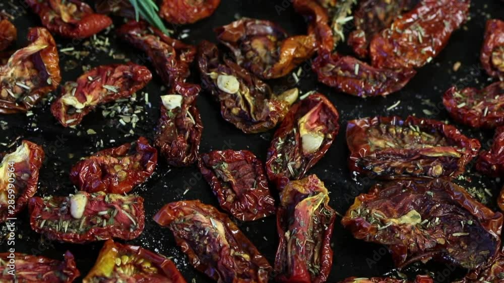 Sun-dried tomatoes with spices and garlic on a baking sheet. On top of them lies fresh rosemary. Vertical movement.