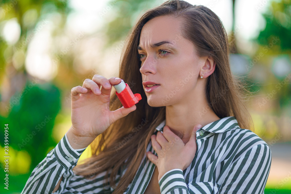 Asthmatic woman using inhaler from an asthma attack in park Asthmatic woman using inhaler from an asthma attack in park