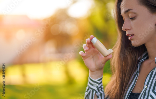 Asthmatic woman using inhaler from an asthma attack outdoor