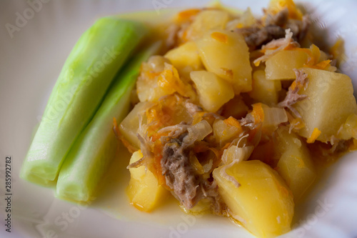 Stewed potatoes with meat. Fresh cucumber. On a white dish.