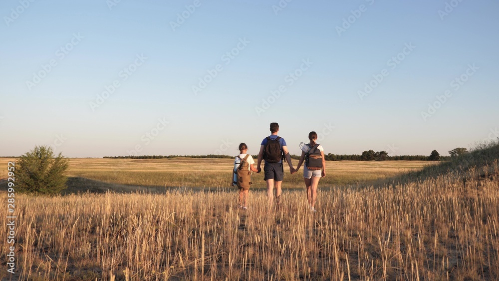 Family of tourists on a journey. Dad with two daughters on camping trip. children and father with backpacks are walking through field. teamwork of tourists. movement towards intended goal and victory