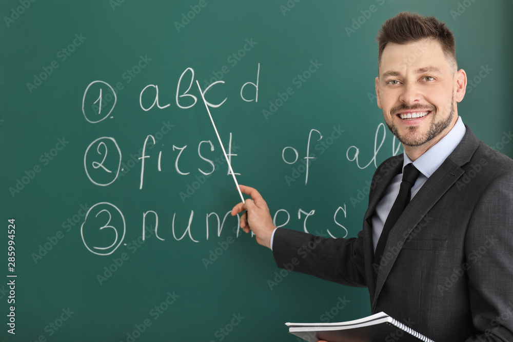 Handsome male teacher near blackboard in classroom