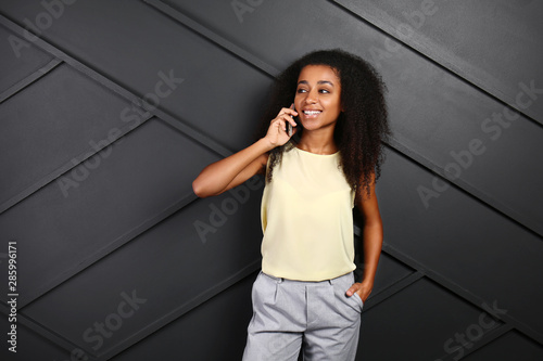 Portrait of beautiful African-American woman talking by mobile phone on dark background