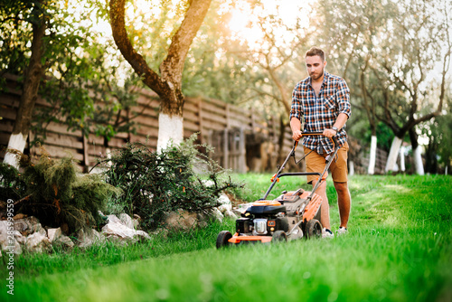Close up details of landscaping and gardening. Worker using industrial manual lawnmower. photo