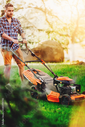 Portrait of handsome gardenere worker using lawnmower and cutting the garden grass