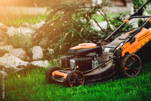 Gardening and landscaping concept - worker, gardener working with lawnmower and cutting grass in garden. photo