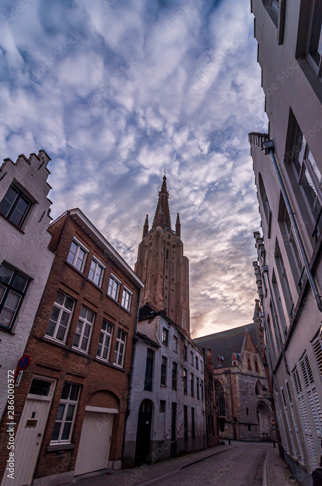 Fototapeta premium Street of Bruges and Church of Our Lady with beautiful cloudy sunrise. Bruges, Belgium