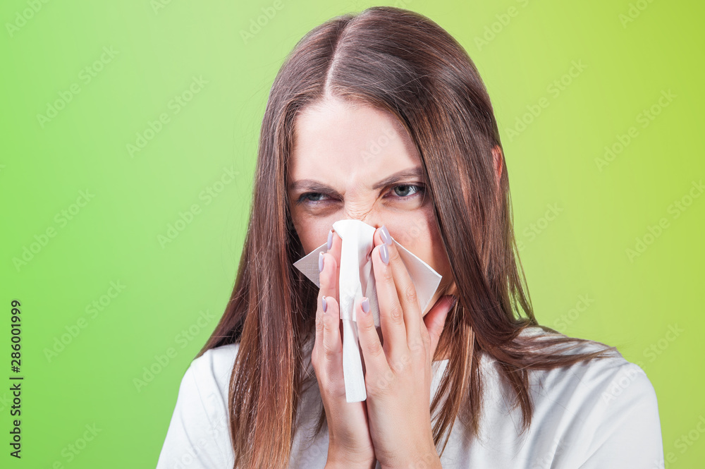 young woman blows her nose in a paper handkerchief on a yellow green background close-up young woman blows her nose in a paper handkerchief on a yellow green background close-up