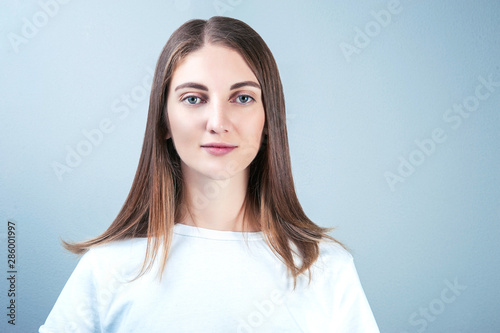 Obraz na plátně a young woman in a white T-shirt against a blue-gray wall looks directly at the camera and smiles easily