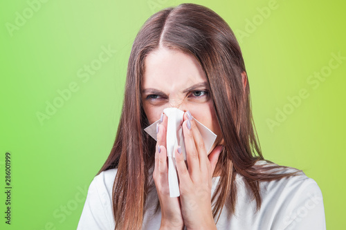 young woman blows her nose in a paper handkerchief on a yellow green background close-up