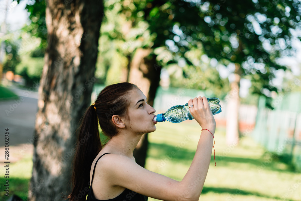 Athlete girl drinks water after a workout in the park Athlete girl drinks water after a workout in the park