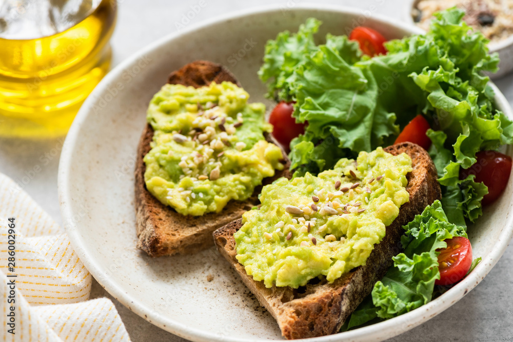 Breakfast avocado toast with seeds and green salad on plate, closeup view Breakfast avocado toast with seeds and green salad on plate, closeup view