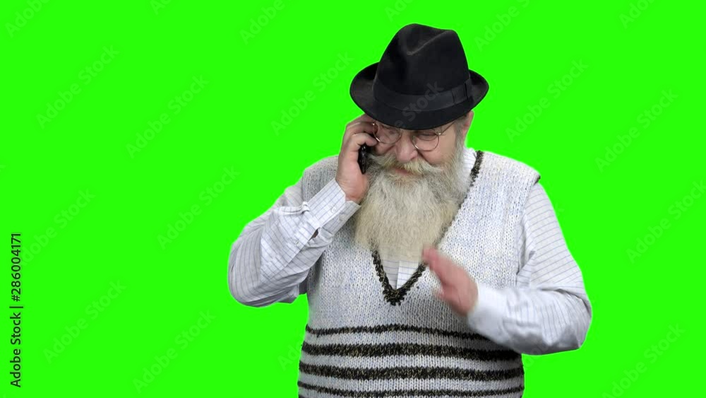 Aged man talking on mobile phone. Senior bearded man in hat talking on cell phone. Green Chroma Key background. Aged man talking on mobile phone. Senior bearded man in hat talking on cell phone. Green Chroma Key background.
